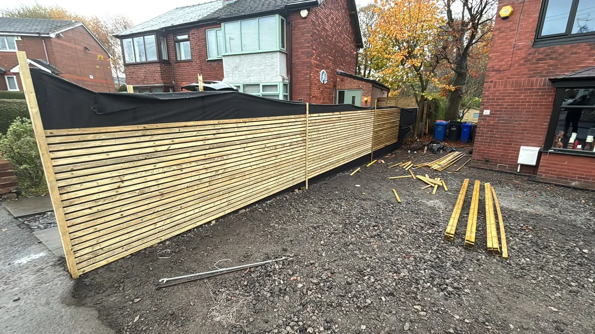 Horizontal slatted timber screen fencing under construction along a driveway boundary